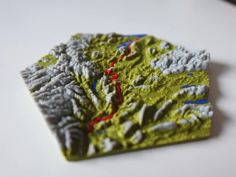 Tištěná terénní mapa s horskými hřebeny, modrými vodními plochami a červenou trasou vedoucí údolím